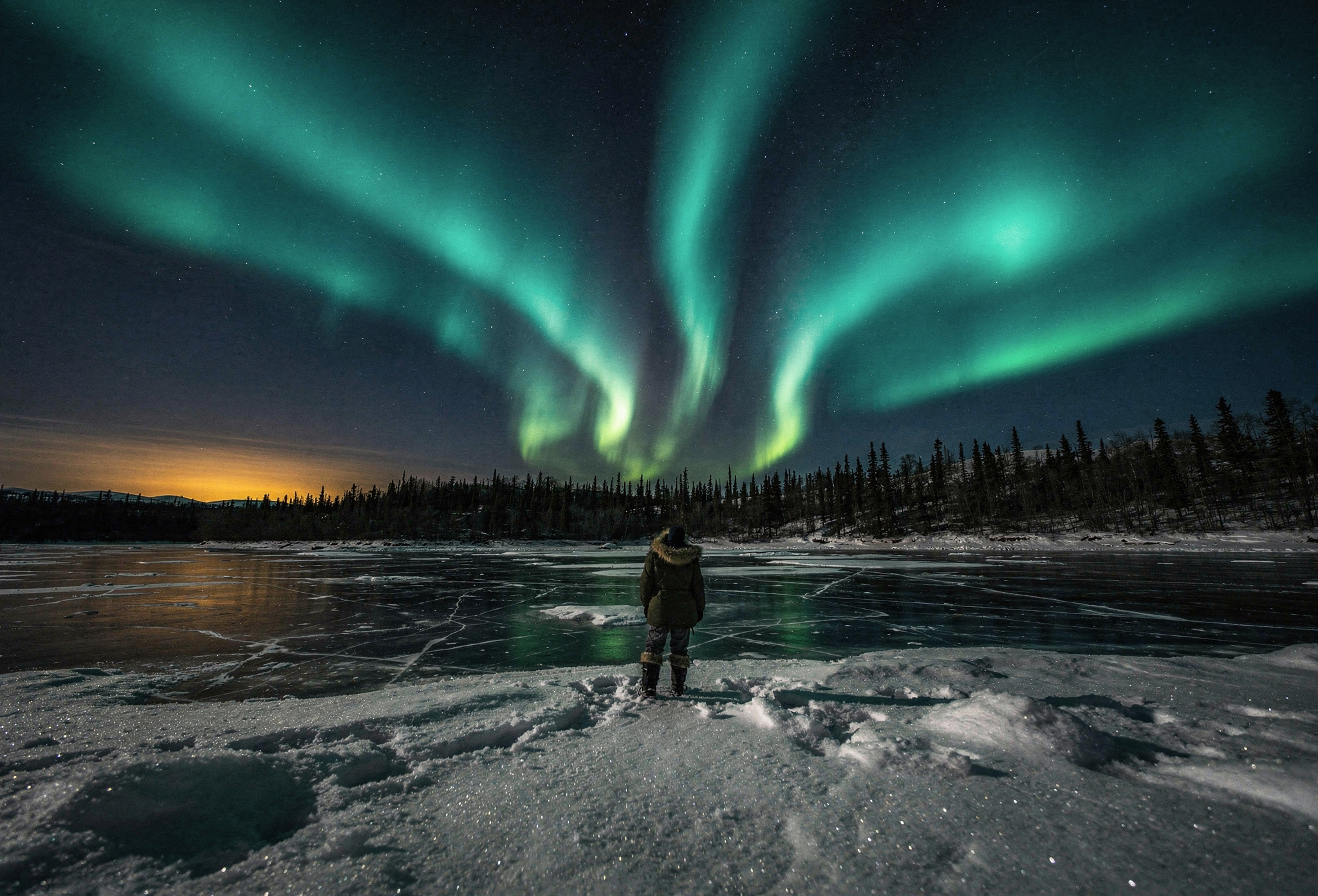 Green and teal aurora swirling over a frozen Yukon lake and spruce forest